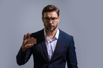 Portrait of serious arrogant proud business man showing plastic credit card against grey background. Business and success concept. Online shopping. On-line payment. Balance on credit card.