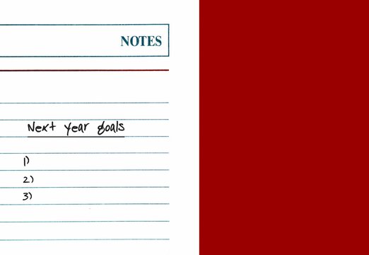 A note paper with text written NEXT YEAR GOALS and blank lists ,on red copy space background - concept of goals setting for the next coming year