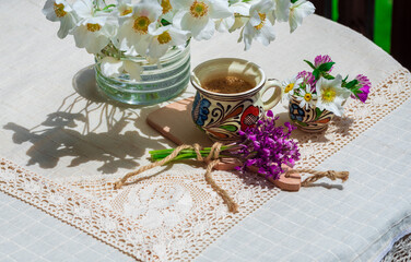 A cup of coffee and spring wildflowers on a white tablecloth.