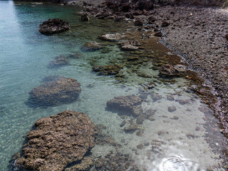 Clear sea water at a beach showing sand and rocks below its surface.