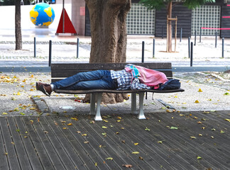 Homeless man with covered face lying on a wooden bench