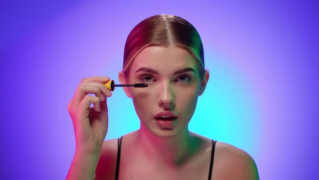 Young nordic female model puts on eyelash makeup with half naked torso, portrait in studio with isolated background