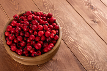 red hawthorn berries in wooden bowl on flat wooden surface.