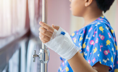 Shot of child patients stand at the window in the hospital are adding saline solution on hand and look outside.