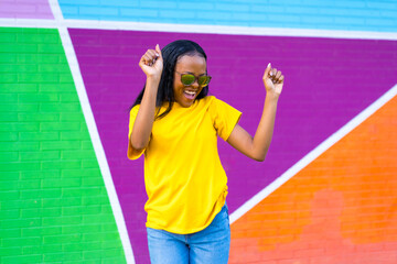 Happy african woman smiling and dancing next to colorful wall