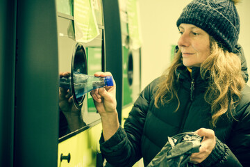 Woman puts bottle in automatic bottle recycling machine. Reverse vending recycling machine.