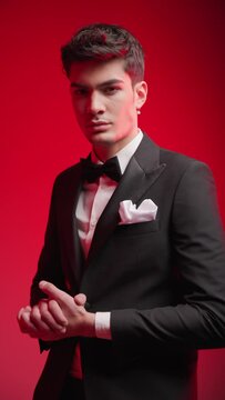 attractive elegant groom wearing black tuxedo with bowtie and handkerchief holding hands and moving in front of grey background