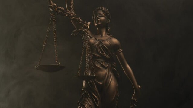 blindfolded bronze statue goddess of justice holding a scale for concept of right and wrong, equality and balance on black background with smoke