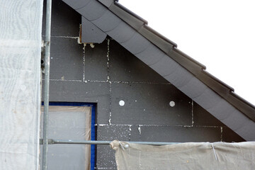 A wall of a house covered with EPS graphite polystyrene boards for thermal insulation, a window covered with a protective film, a scaffolding