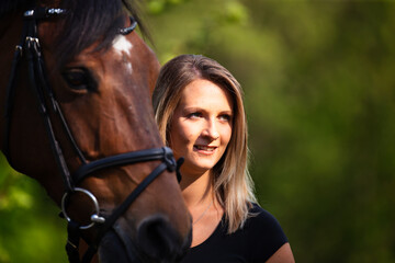 Young brunette woman in head portrait next to her horse. Sharp main subject.