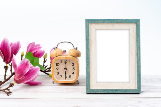 Blank picture frame and alarm clock on wooden floor with copy space.
