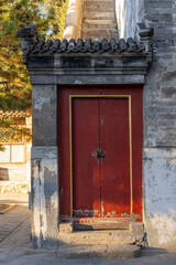 A close up view of a red door with Chinese architectural design leading to a stone staircase with an outer wall that conceal anyone climbing from the side view.