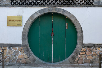 A circular green door with circular stone frame over a white wall and with Chinese writings that translate "Summer Palace Mini Fire Station" and "Staff Lounge."