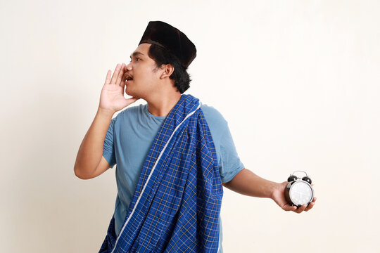 Asian muslim boy standing shouting to beside while holding a alarm clock
