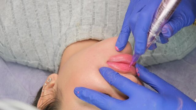 Young woman having permanent makeup on lips in beautician salon. Close up