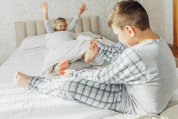 the children are wrapped in a blanket and tickling each other's heels on the bed. Family having fun...