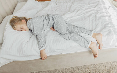 A little blonde girl sleeps sweetly in bed with white linen and pajamas. place for text. healthy...