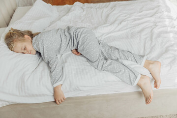 A little blonde girl sleeps sweetly in bed with white linen and pajamas. place for text. healthy...