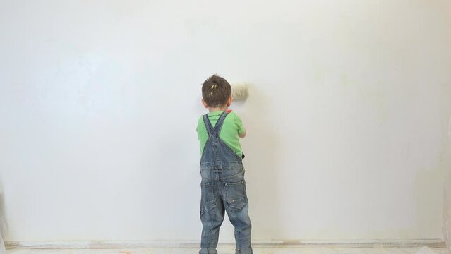 Little kid with big brush roller painting the wall in white