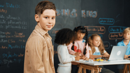 Smart boy smiling at camera while diverse friend working or learning engineering code or prompt in...