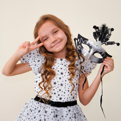 Child in a carnival masquerade mask. Festival, carnival, party. A little girl makes faces in a...