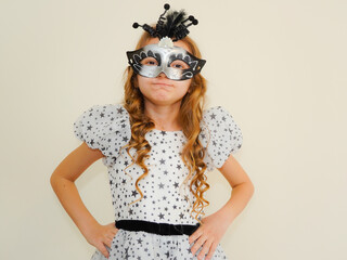 Child in a carnival masquerade mask. Festival, carnival, party. A little girl makes faces in a...