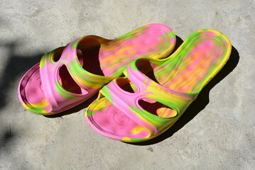 Women's summer shoes are arranged on a cement background. Pink, bright, multi-colored flip-flops...