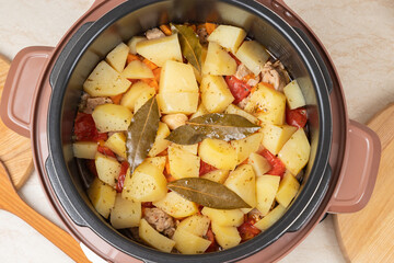 Modern, bright light multi cooker with just cooked stewed potatoes with meat on the kitchen table. Top view of multi cooker with just cooked dish.