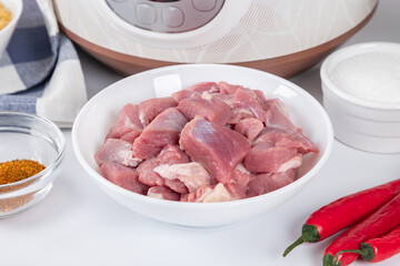 Prepared meat and other ingredients ingredients for cooking pilaf in modern multi cooker in kitchen on a table. Cooking pilau with meat in multicooker.