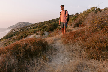 Hiker man walking on ocean coastline with warm sun light.