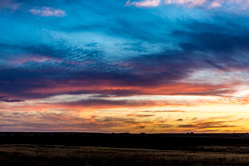 Sunrise or sunset in the Russian steppe at golden hour. Stratus, Cirrocumulus and Altocumulus clouds. The sun is shining from behind a cloud. Red orange and white shades. Morning or evening.
