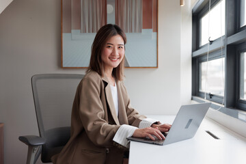 Happy brunette business lady using laptop, smiling at camera, posing for work, sitting in office in modern office Successful entrepreneurs and careers ke