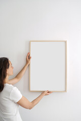 Woman hanging copy space poster in wooden picture frame on white wall