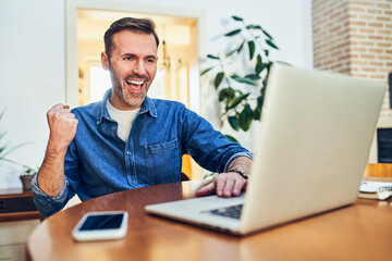 Excited adult man celebrating online investment success using laptop at home
