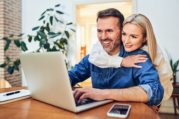 Happy adult couple at home using laptop together