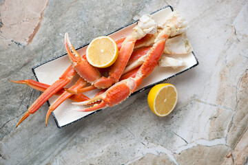 Plate with boiled opilio or snow crab and lemon, top view on a light-grey granite background,...