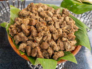 A large pile of cooked beef cube chunks served in a brown clay bowl with a green banana leave base.