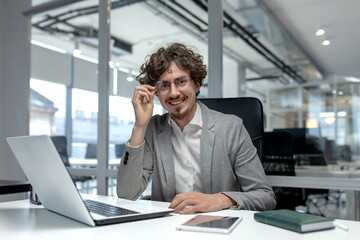 Portrait of a young smiling and successful young man sitting in the office at a desk and working on...