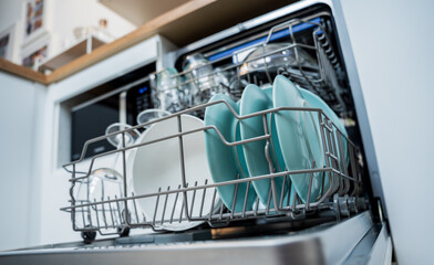 The white kitchen and opened dishwasher with clean dishes