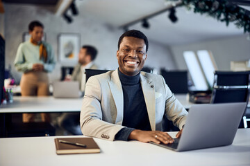 Portrait of a smiling black man, dressed elegantly, working at the office, over the laptop.