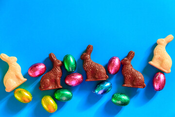 Easter chocolate eggs in foil and Easter chocolate bunnies on blue background. Top view