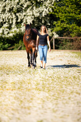 Young woman with a black shirt and short highlighted hair stands with her horse on a sunny riding arena.