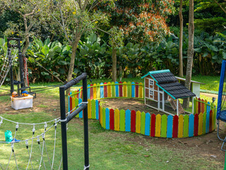 A medium sized pet house with a colorful fence surrounding its area, in an outdoor playground.