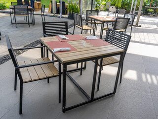 Three sets of empty outdoor dining tables with black metal and wooden materials and red dining mat.