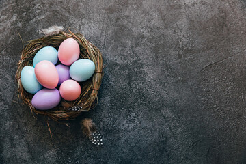 Happy Easter concept. Preparation for holiday. Colorful pastel decorated easter eggs in nest on grunge scratched dark black shale background. Simple minimalism flat lay top view copy space - Powered by Adobe