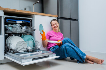 Young woman sitting on the floor near the dishwasher machine