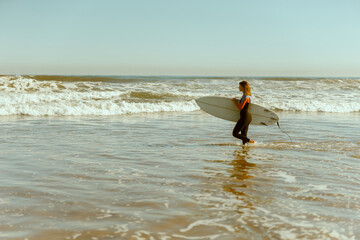 Side view of female surfer in wetsuit with his surfboard entering the sea for riding on waves