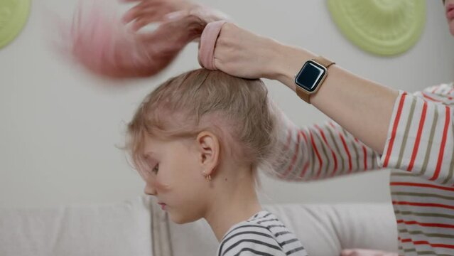 A young woman putting scrunchy in a playful rose-haired girl hair while sitting on a light sofa.