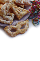 Italian sweet crisp pastry deep-fried and sprinkled with sugar in shape of Carnival mask on colorful plates on white. Chiacchere or crostoli, bugie, cenci with confetti and paper serpentine