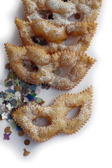 Italian sweet crisp pastry deep-fried and sprinkled with sugar in shape of Carnival mask isolated on white background. Chiacchere or crostoli, bugie, cenci with confetti and paper serpentine